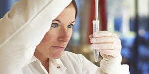 Person in white lab coat pipetting into a tube